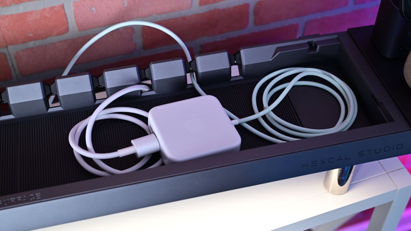 A coiled white cable with square adapter rests in a dark tray labeled Hexcal Studio. Background shows a red brick wall.