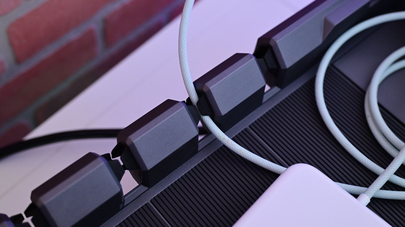 Close-up of a row of upright plastic Lego bricks against a ridged surface, with a coiled gray cable passing through gaps and a red brick background.