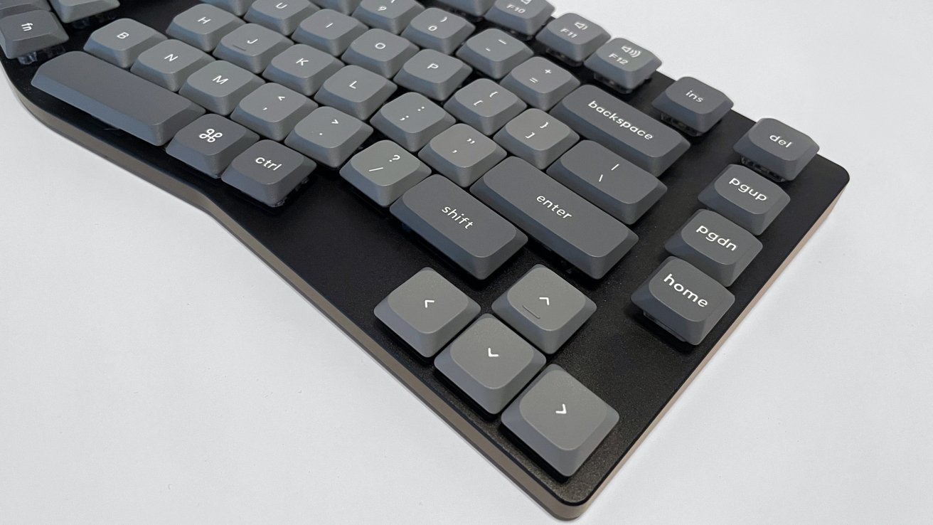 Ergonomic keyboard with gray keys and white lettering, featuring arrow keys, enter, shift, and command key, on a black base.