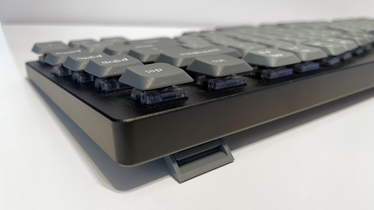 Close-up of a black keyboard with gray hexagonal keys on a white surface, showing an extended kickstand for angle adjustment.