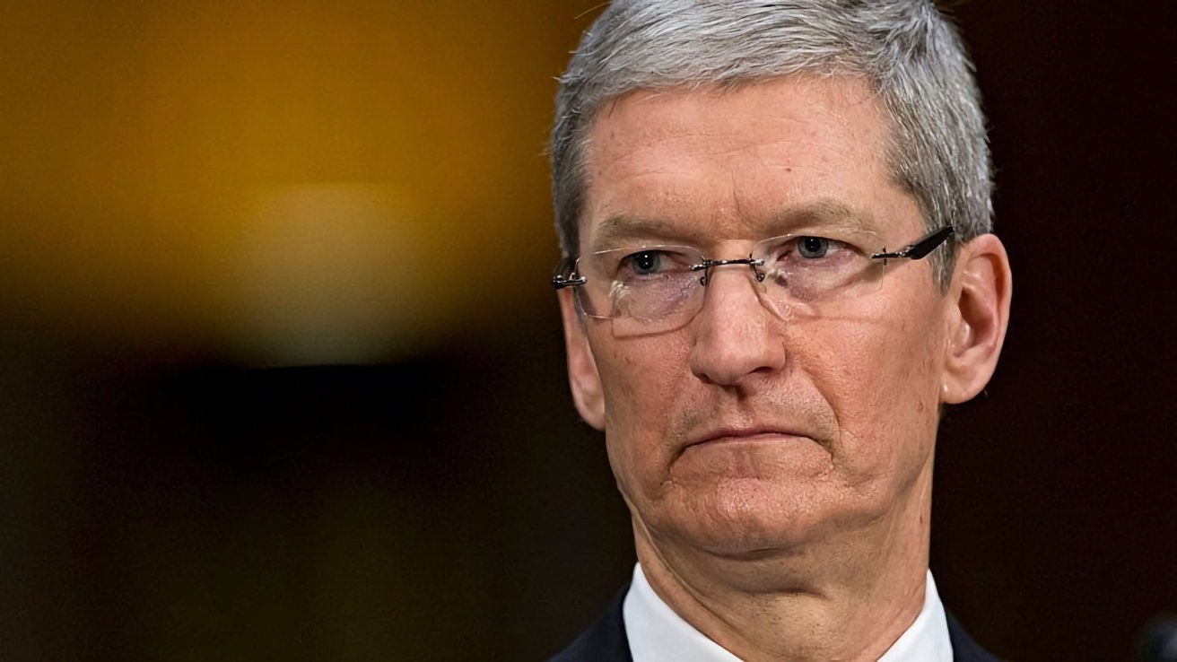 Apple CEO Tim Cook with short gray hair and glasses looks serious against a blurred yellow background.