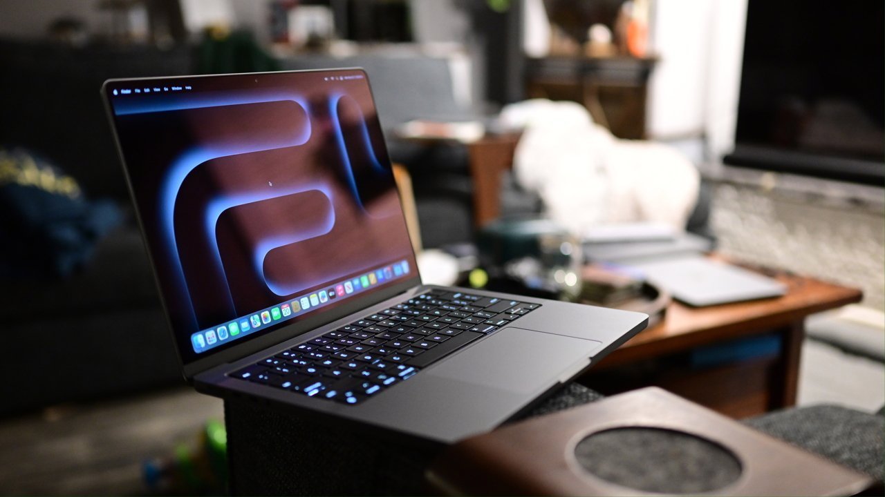Laptop with a glowing keyboard on a couch, displaying an abstract pattern on the screen, in a cozy living room setting with a table and blurred background.