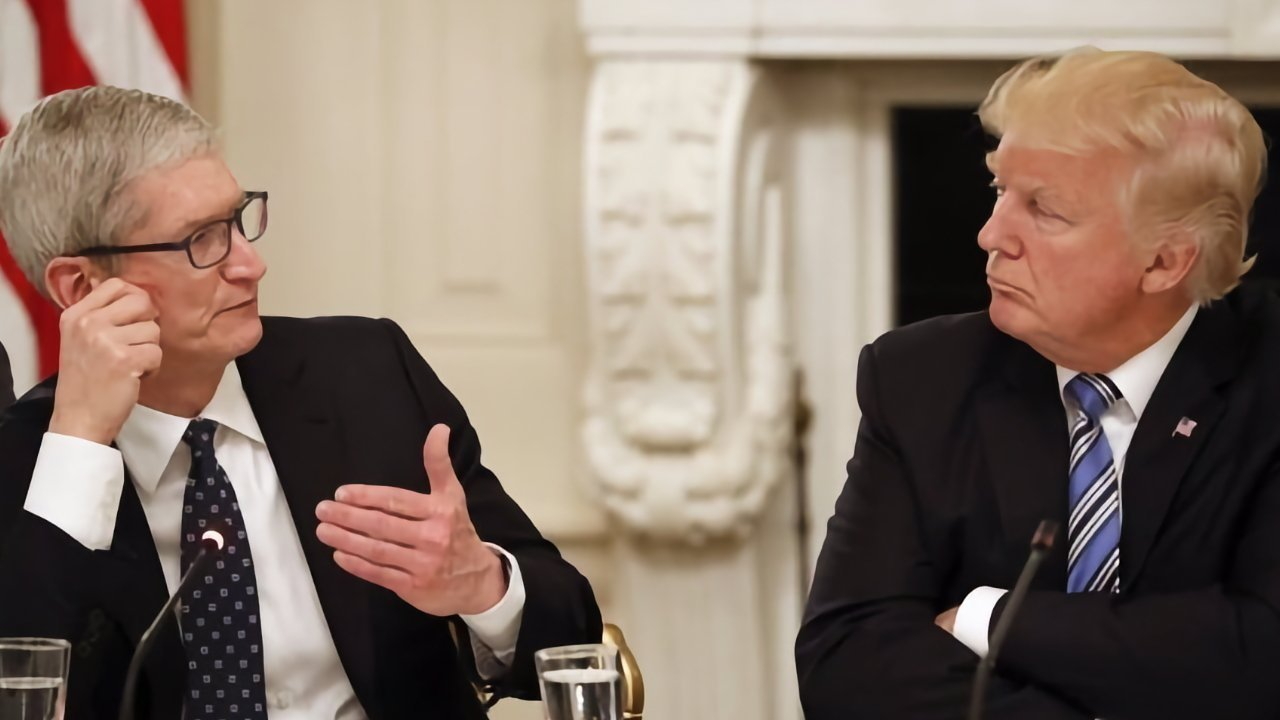 Two men in suits sit at a table, engaged in conversation, with an elegant, ornately decorated background.