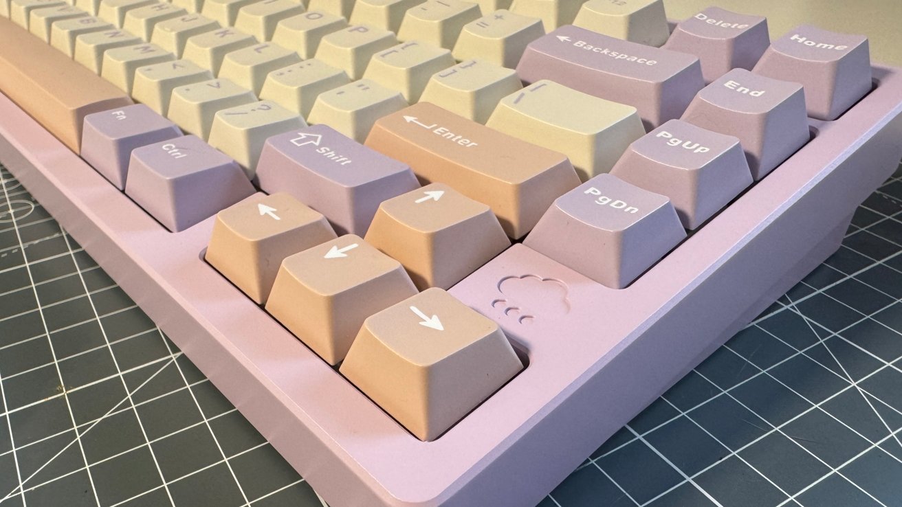 Pastel-colored mechanical keyboard with beige, peach, and lavender keys on a gray grid-patterned surface. The arrow keys feature a cloud design.