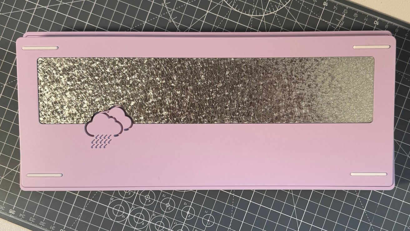 Pink rectangular object with a textured metallic strip and cloud with rain design on a grid-patterned surface.
