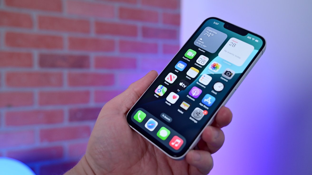 Holding up an iPhone against a purple and blue wall showing the screen full of icons