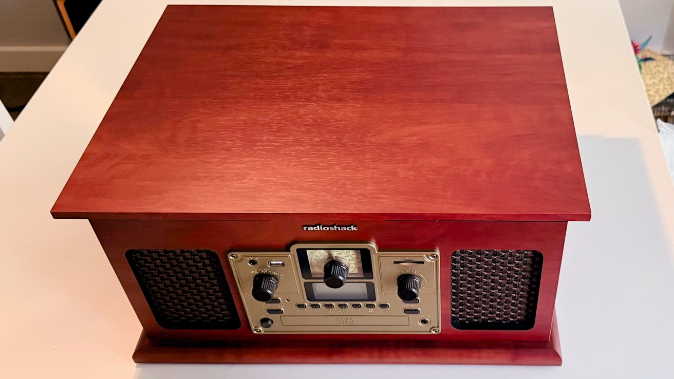 Vintage-style wooden tabletop radio with a central control panel featuring knobs and dials, flanked by speaker grills on either side.