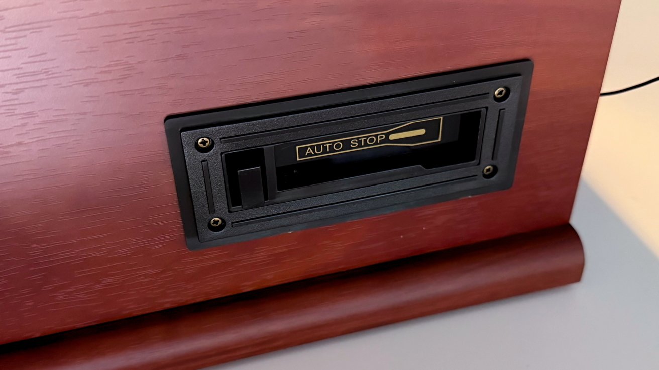 Close-up of a wooden device with a black switch labeled 'AUTO STOP' in gold, set in a rectangular frame with four screws.