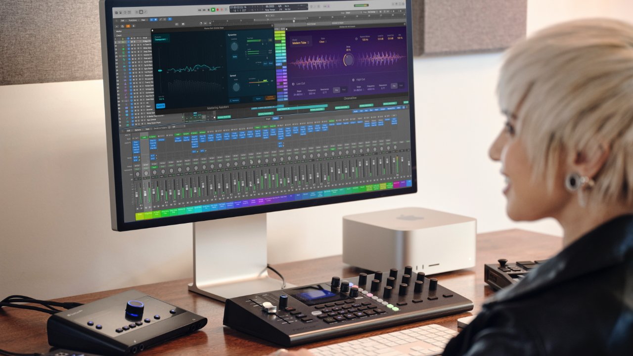 Person with short hair using audio mixing software on a desktop computer, with audio equipment on the desk in a well-lit room.
