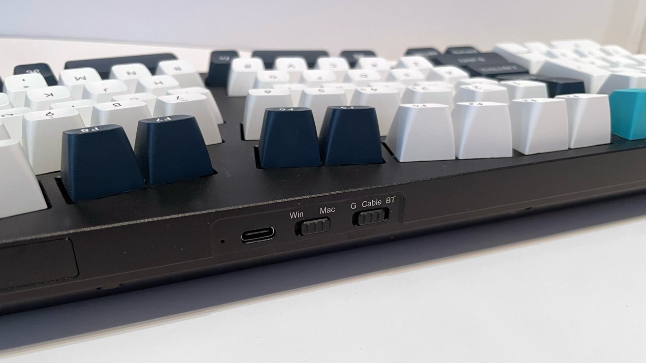 Close-up of a keyboard with white and blue keys, USB-C port, and toggle switches labeled Win, Mac, G Cable, BT on a black base.