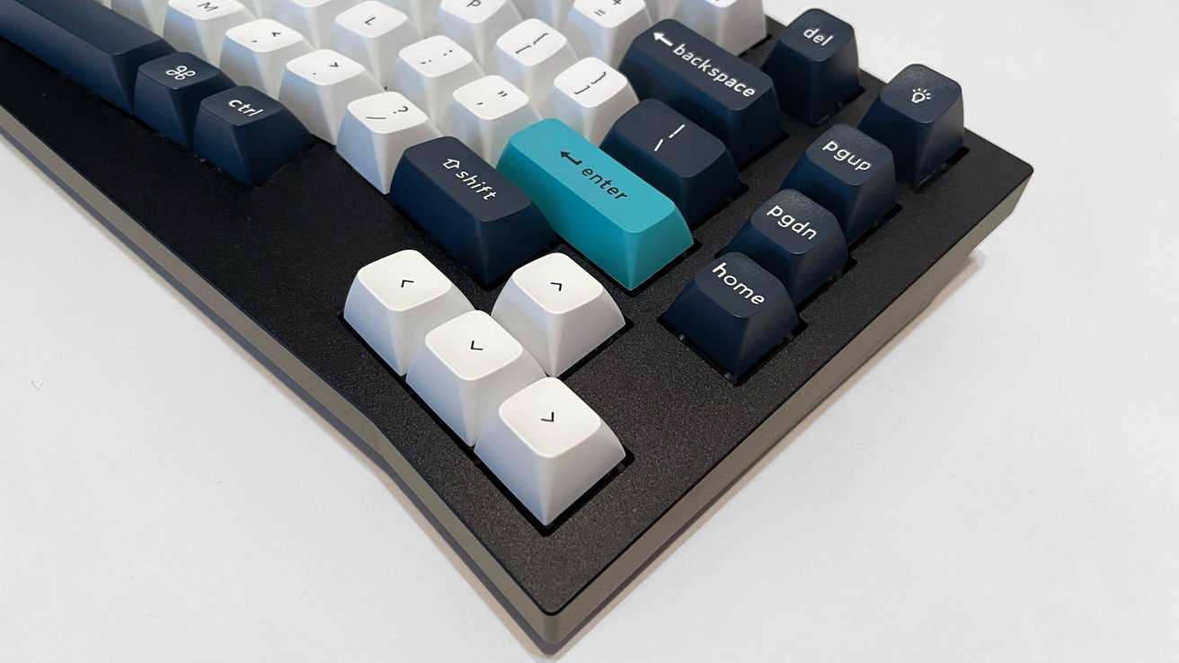 A mechanical keyboard with white, dark blue, and one teal key, featuring various function and navigation keys on a black frame.