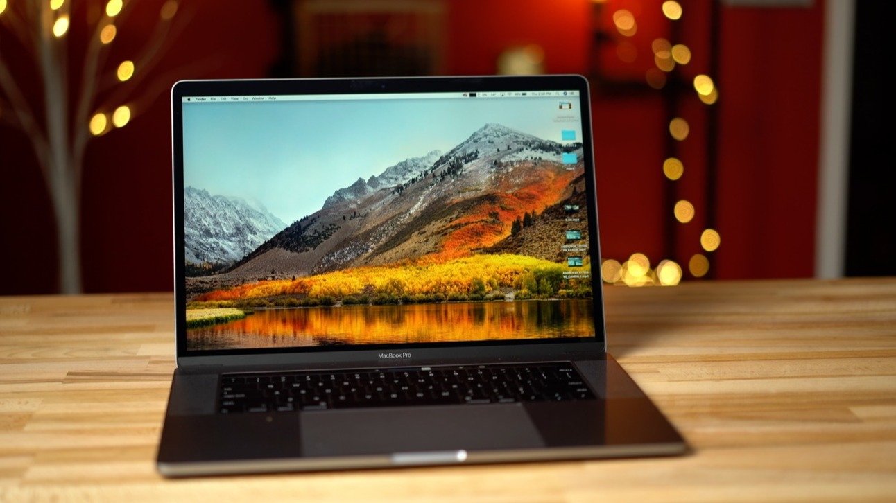 Laptop with mountain landscape wallpaper on wooden table; soft bokeh lights in background.