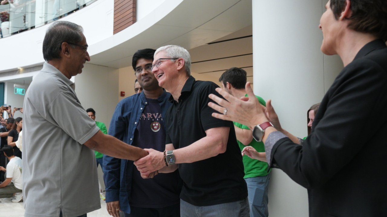 A group of people in a modern building; one man shakes hands while others smile and clap, creating a friendly atmosphere.