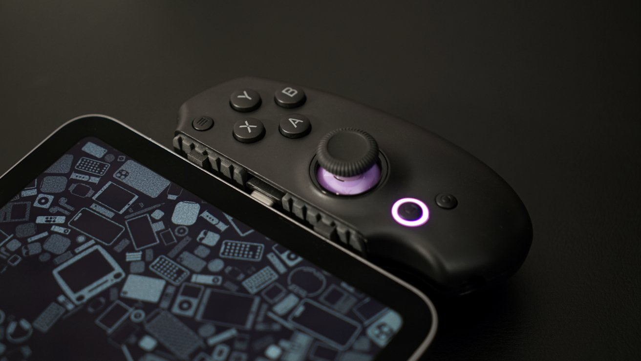 Tablet with a geometric patterned screen and attached black gaming controller featuring buttons and a joystick on a dark surface.