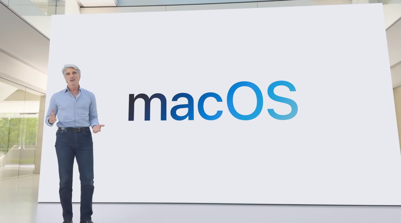 A person in a blue shirt and jeans stands in front of a large screen displaying the word 'macOS'.