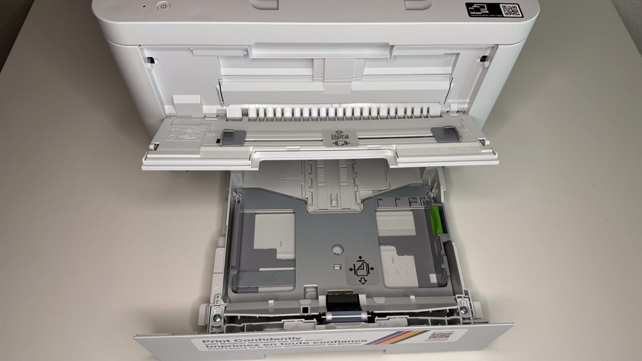 Open printer paper tray showing paper size guides and a QR code on a white surface.