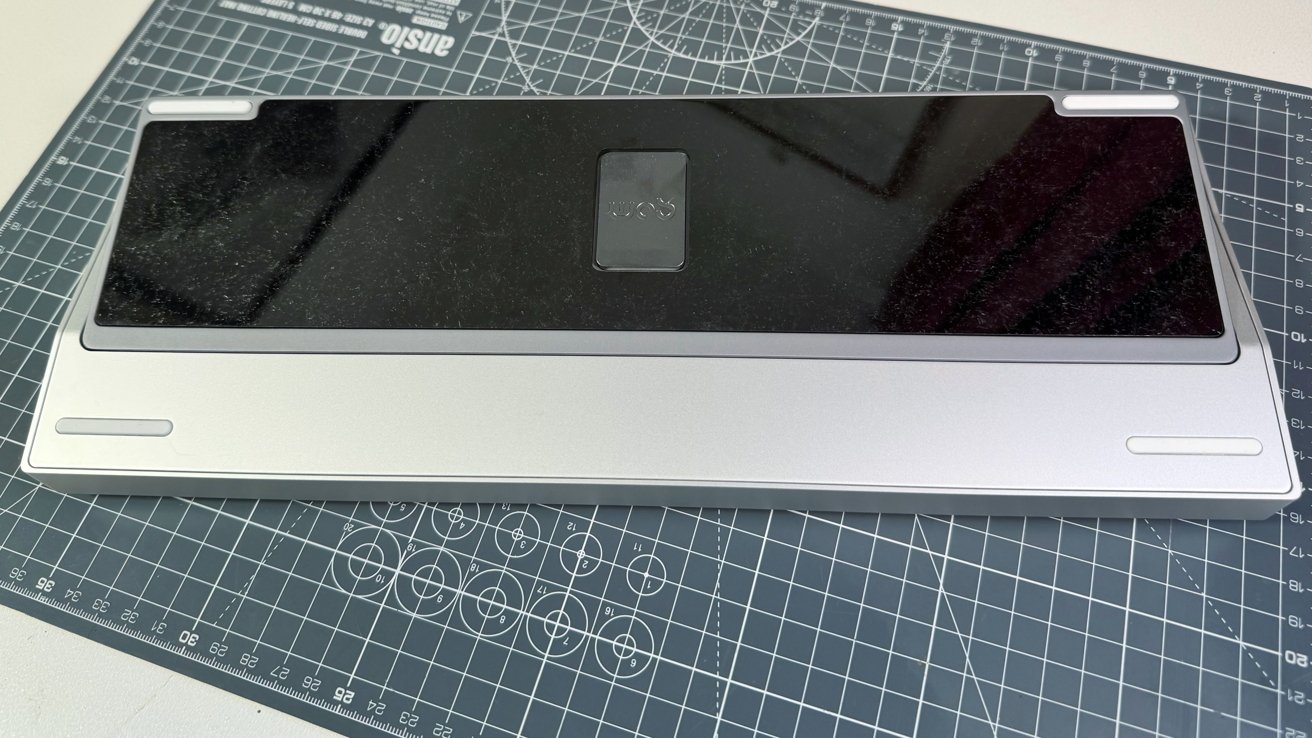 A silver electronic device with a black surface positioned on a grid-lined cutting mat with measurement markings.