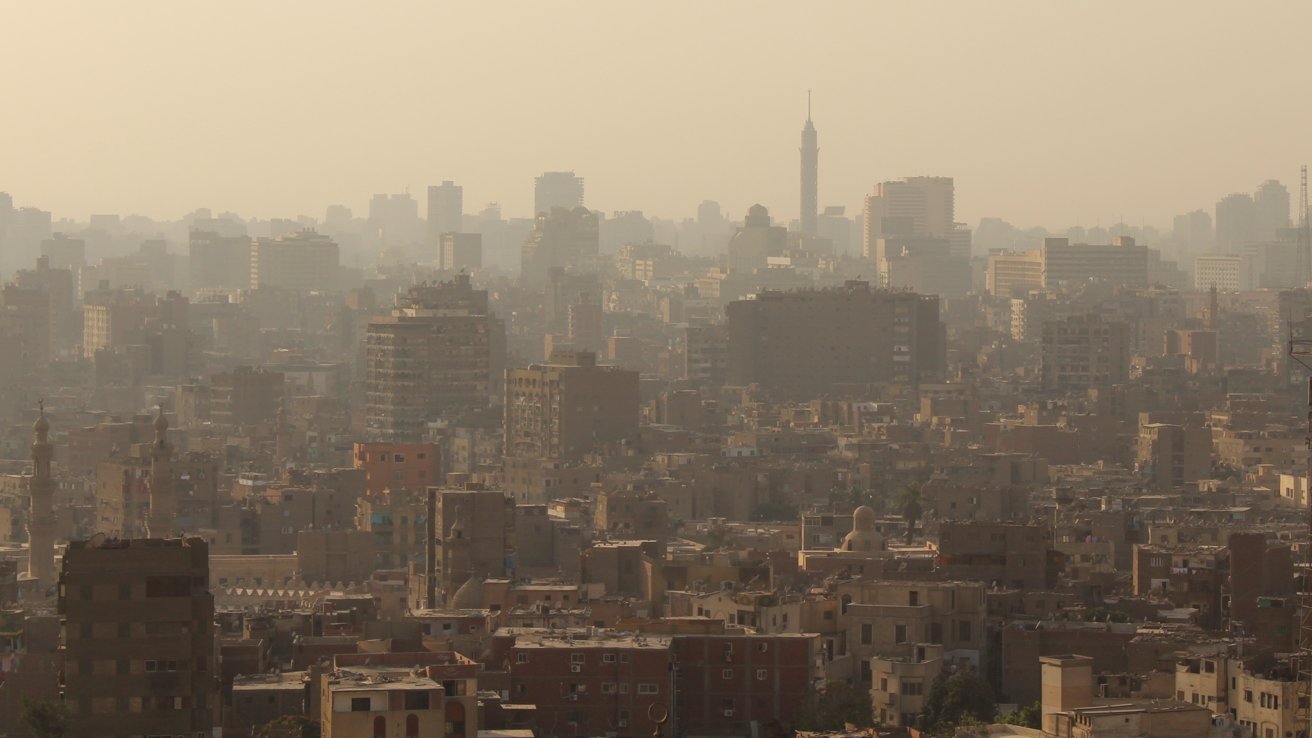 Distant view of a city skyline with numerous tall buildings and a prominent tower against a hazy sky.