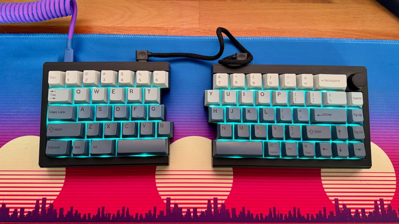 Split keyboard with blue backlight on colorful pad displaying city skyline and sunset design.