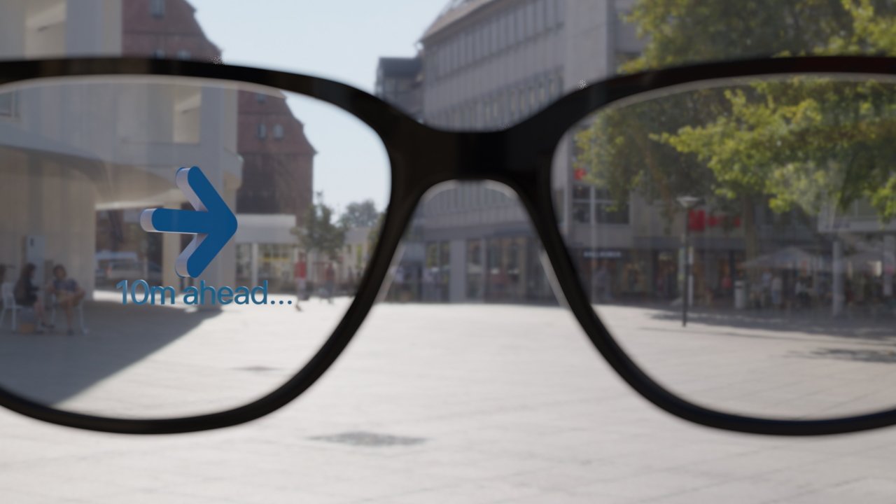 View through smart glasses displaying a digital arrow pointing forward with '10m ahead' text, set against an urban street background.