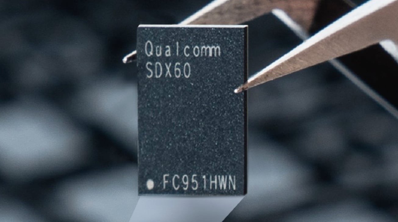 Close-up of a metal tweezer holding a small black microchip labeled 'Qualcomm SDX60' with blurred background.