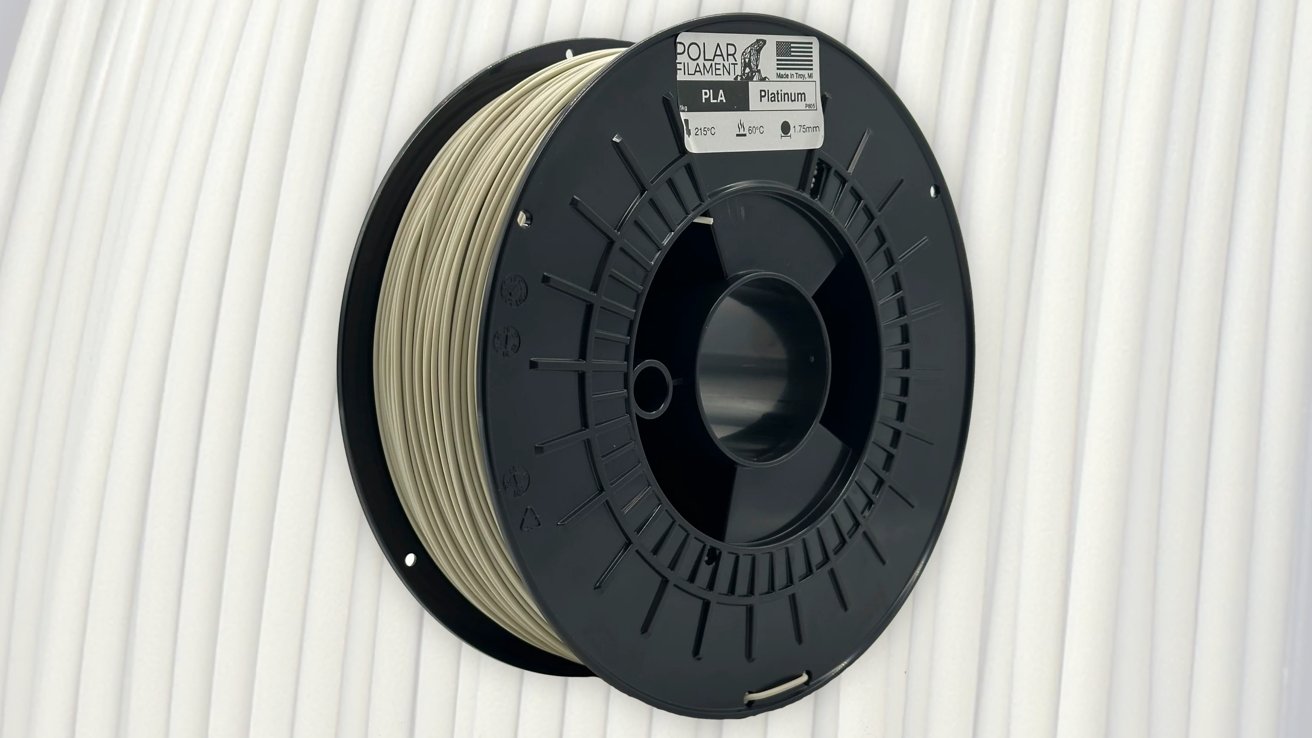Black spool of platinum-colored PLA filament against a textured white background.