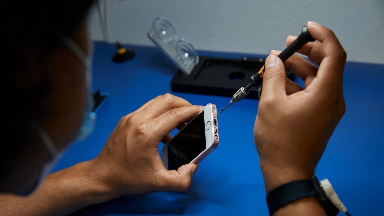 Person using a screwdriver to repair a smartphone on a blue table with repair tools in the background.