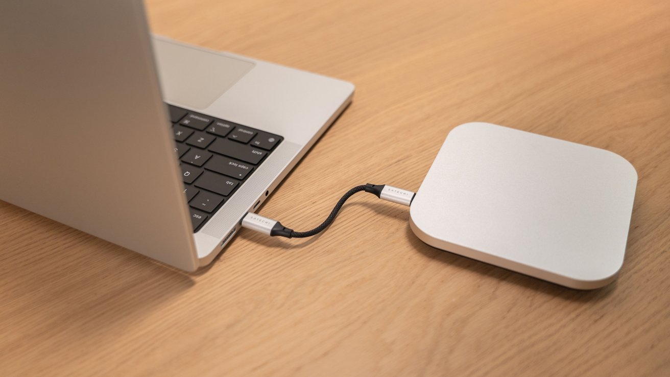 Laptop connected to a small, rectangular external device on a wooden table using a short, black cable.