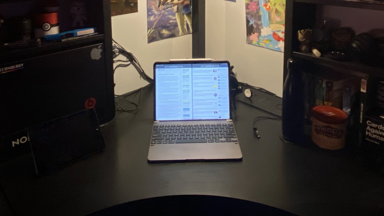 Laptop with split-screen display on a black desk surrounded by shelves with various items and colorful wall posters.