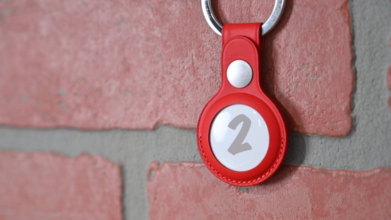 Red keychain with a circular holder displaying the number 2, attached to a metal ring, hanging on a red brick wall.