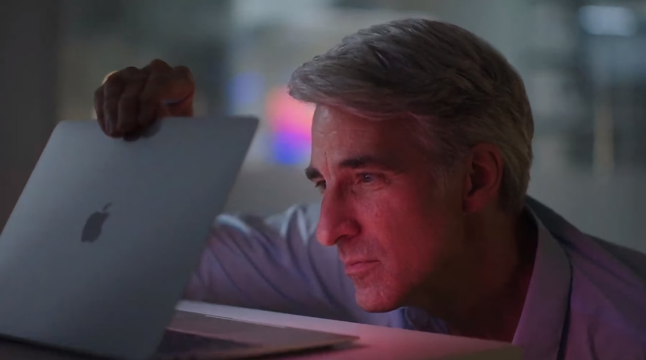 Person with gray hair intently examines a laptop with an Apple logo, in a dimly lit environment.
