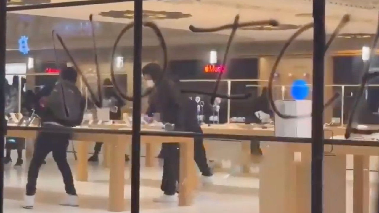 Store interior with people interacting with displays. Large graffiti letters on the window obstruct the view. Brightly lit space and modern technology visible inside.