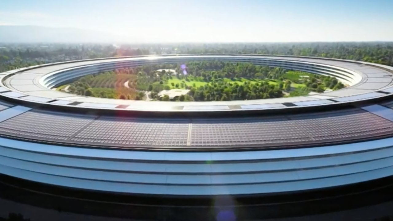 Circular building with solar panels and open green space in the center, surrounded by trees and a clear blue sky in the background.