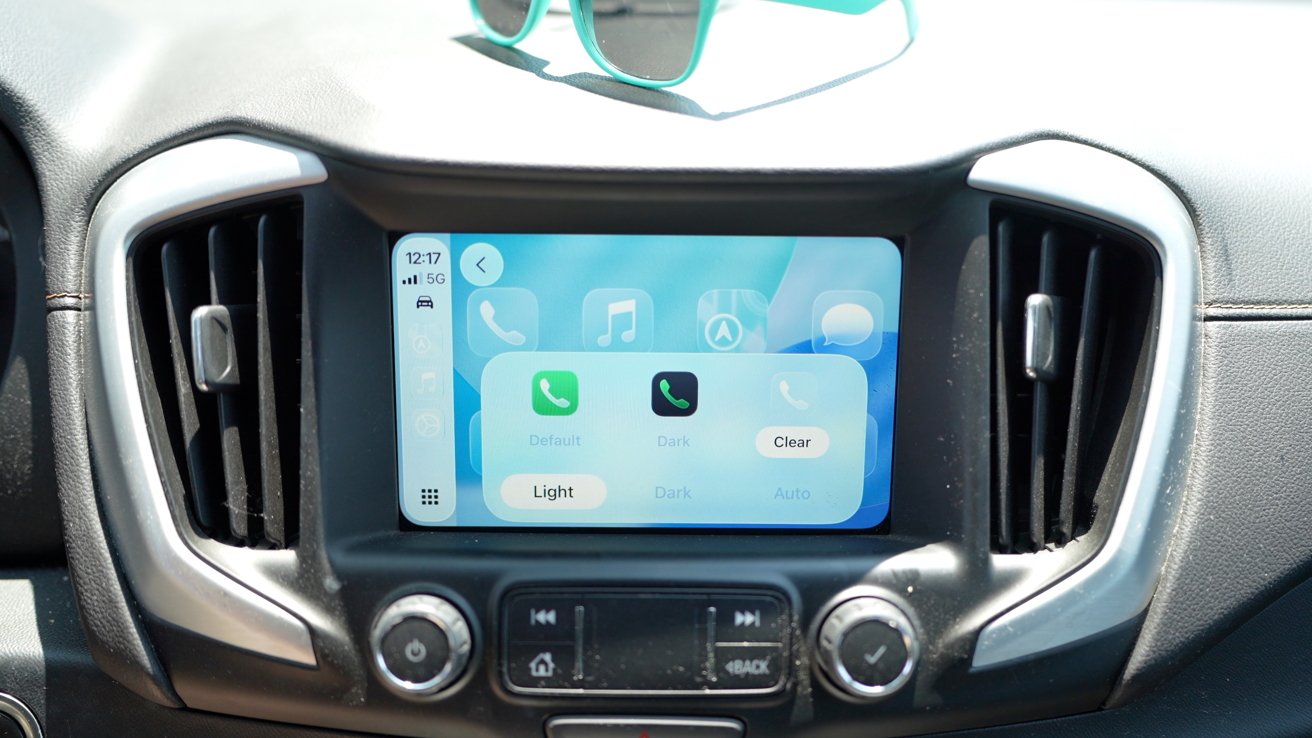 Car dashboard with a touchscreen displaying phone controls and settings. Sunglasses rest on the dashboard above the screen.