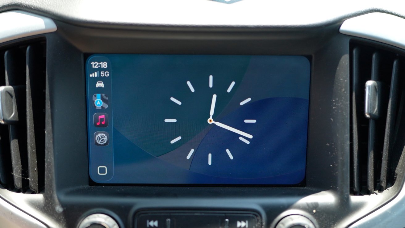 Car dashboard screen displaying 12:18 and signal strength, with app icons on the left and a clock face on the right against a blue and purple background.