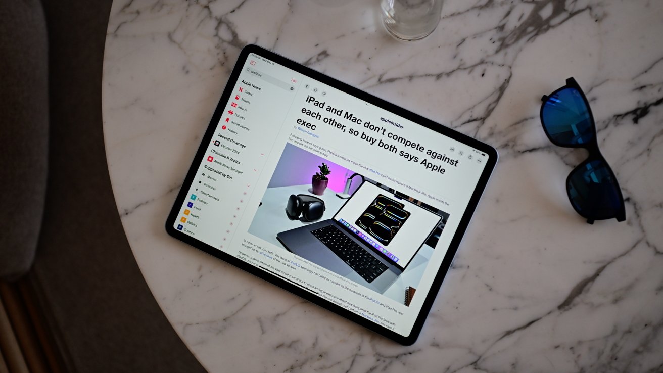 Tablet displaying article about Apple products on a marble table with blue sunglasses nearby.