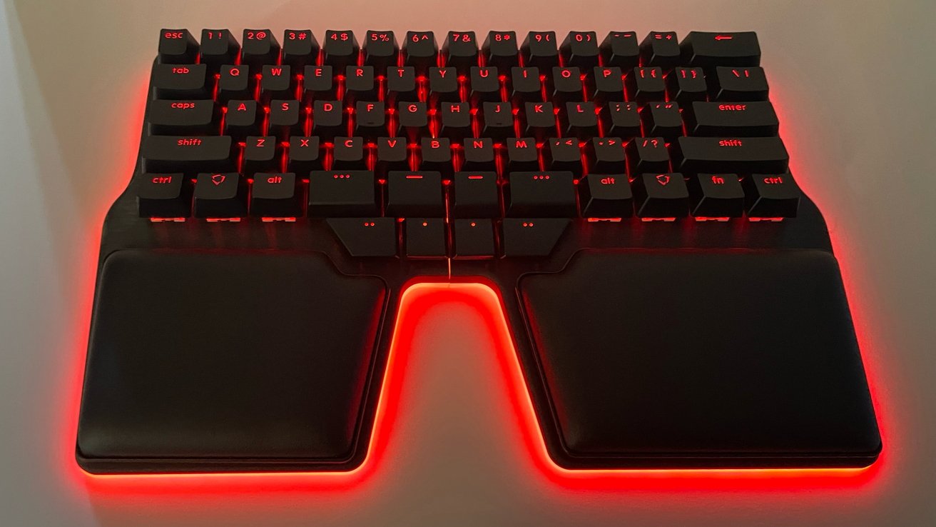 Split ergonomic keyboard with red backlighting, featuring black keycaps and wrist rests, creating a modern, vibrant look.