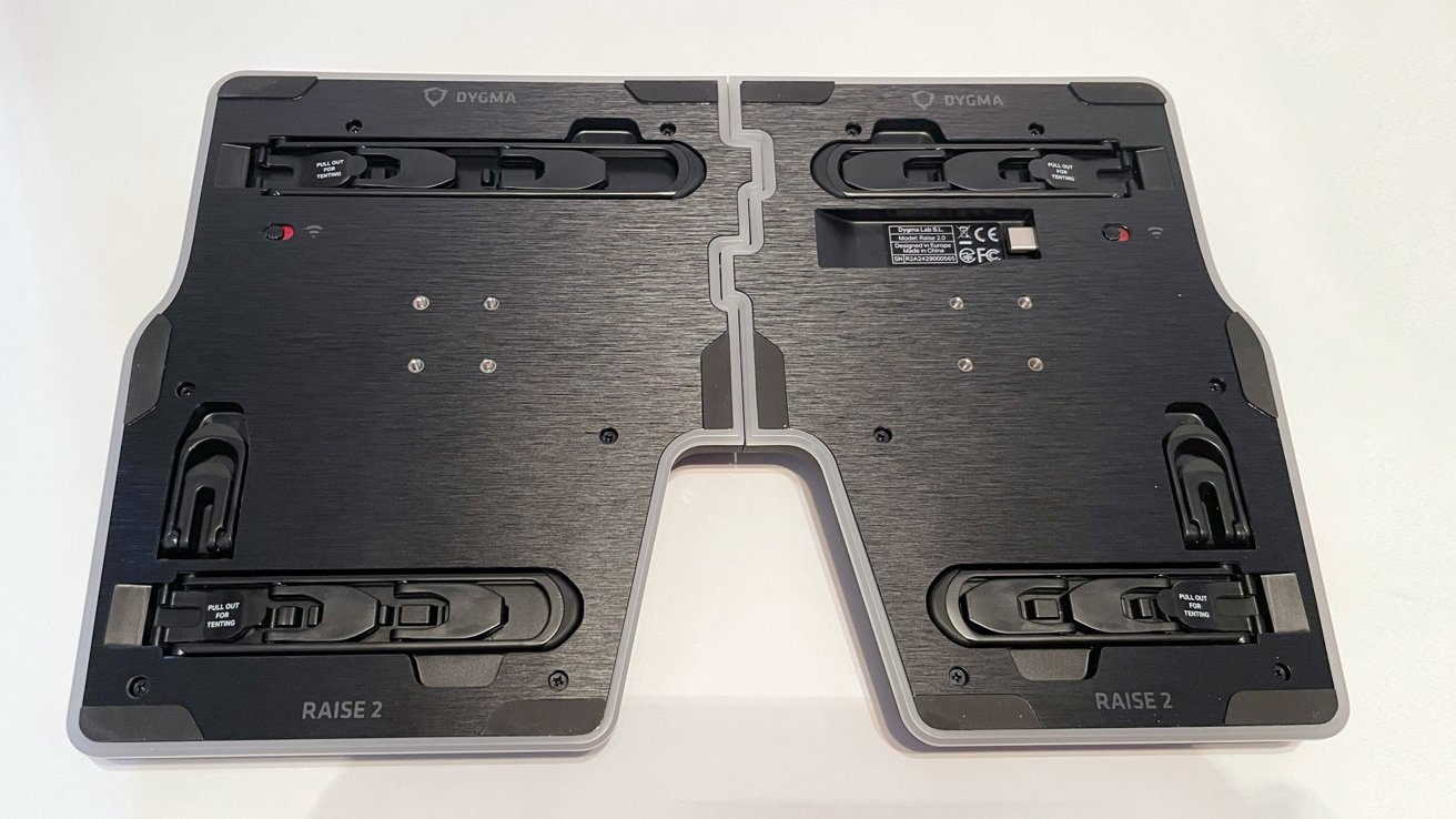 A split keyboard's underside with adjustment mechanisms, featuring black panels and visible brand logo, placed on a white background.