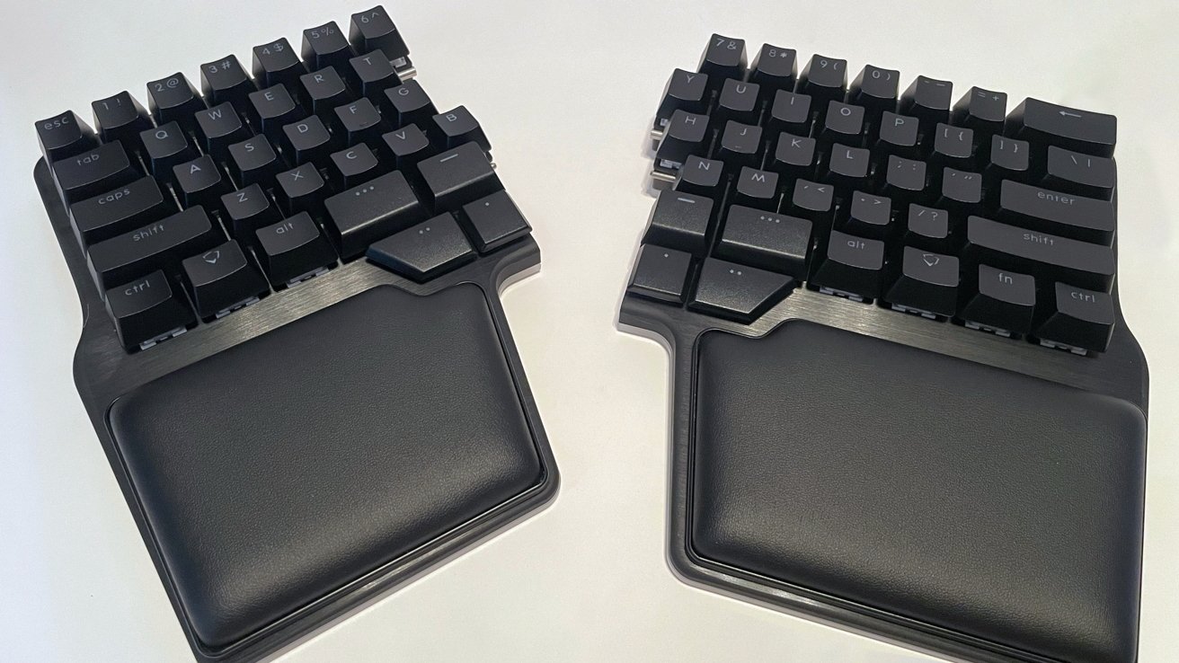 Black split keyboard with two halves, featuring ergonomic wrist supports, on a white surface.