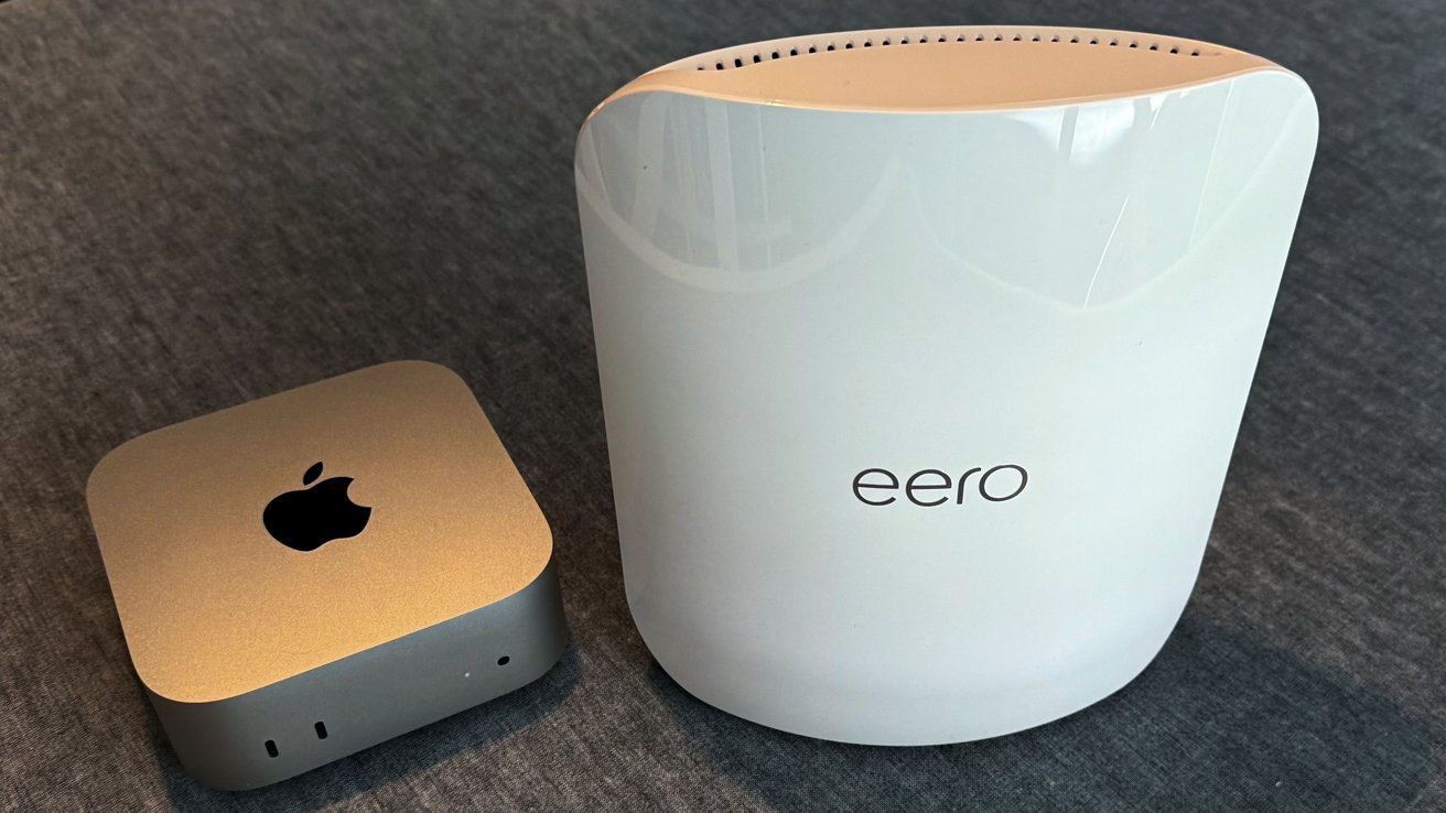 Silver device with an apple logo and a white, curved router labeled 'eero' on a gray surface.