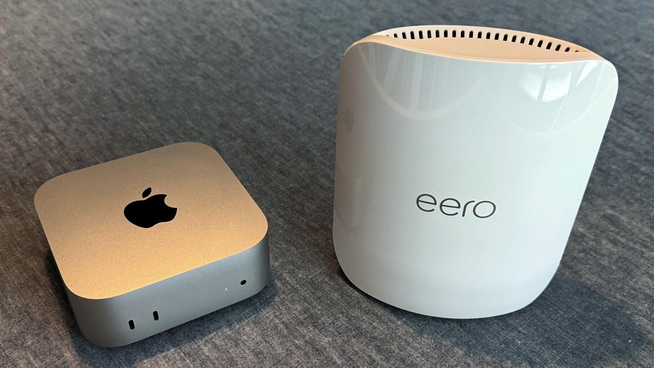 Two devices on a gray surface: a silver, square electronic device with an apple logo and a tall, white, rounded device labeled eero with ventilation slits.