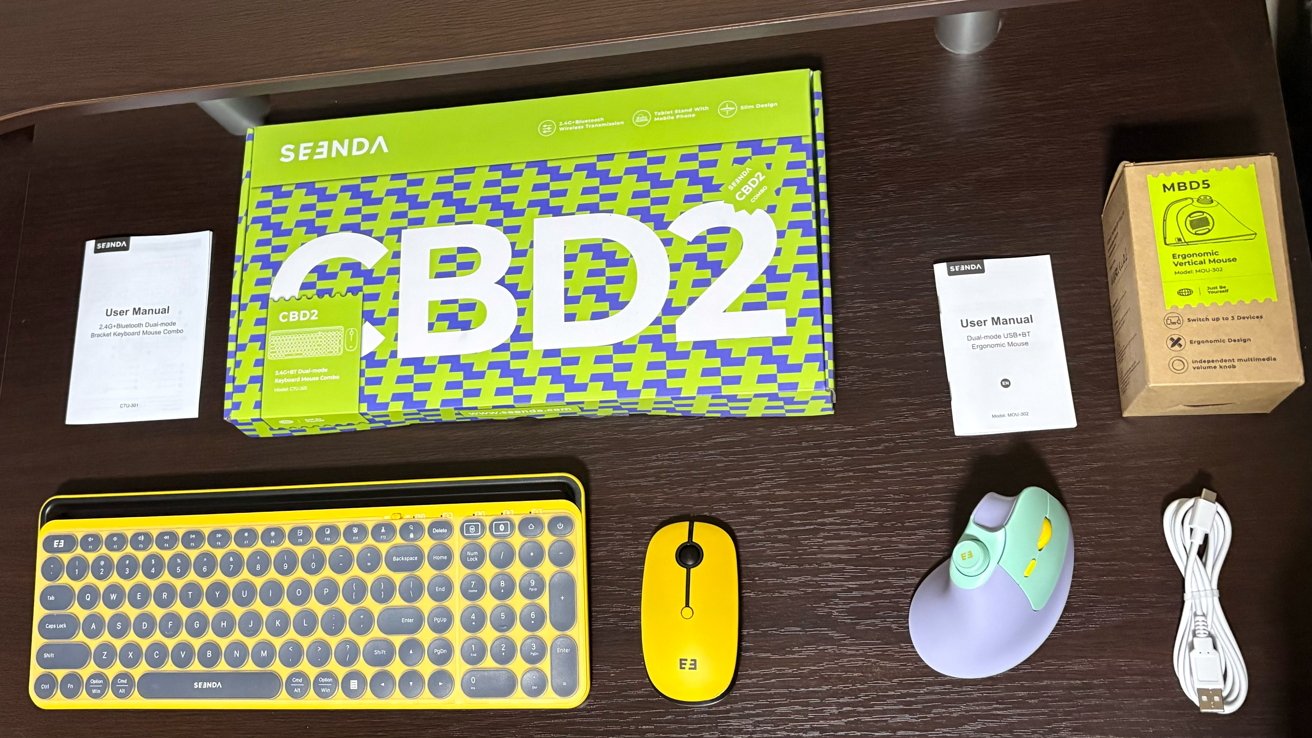 Keyboard and mouse set with colorful designs, two user manuals, packaging, and a USB cable arranged on a wooden surface.
