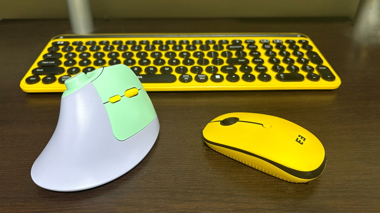 Yellow keyboard, a vertical ergonomic mouse with pastel green and purple colors, and a standard yellow mouse on a dark wooden desk.
