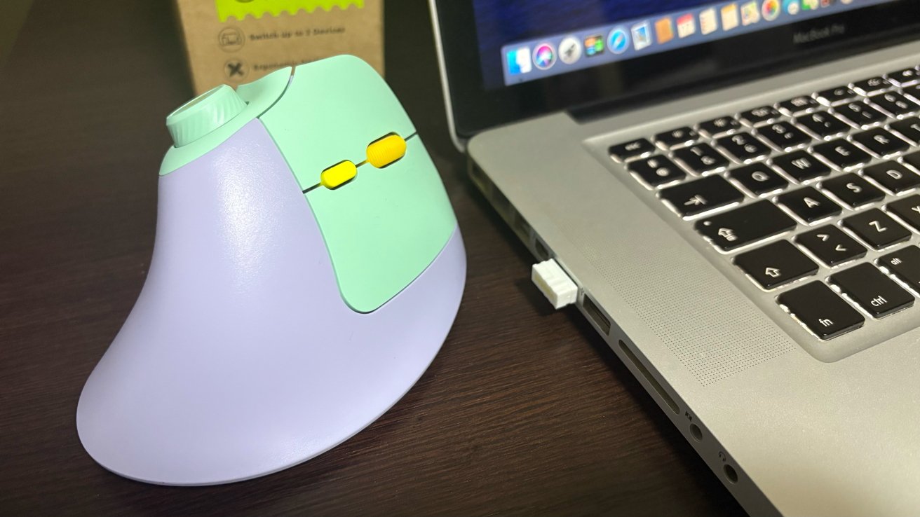 Ergonomic vertical mouse with green and purple design next to a silver laptop on a dark wooden table.
