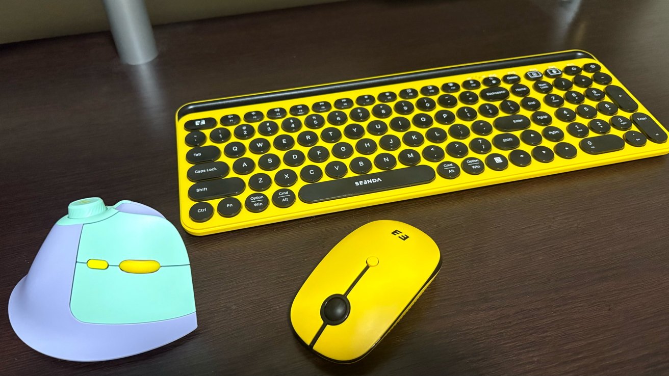 Yellow keyboard and matching mouse on a dark wood desk, with a colorful ergonomic mouse on the left.