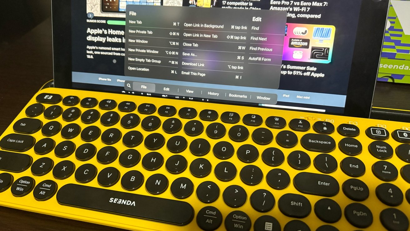 Yellow wireless keyboard with round black keys in front of an open laptop displaying a web browser menu.