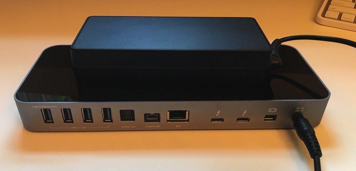 一个时尚的电子扩展坞，带有多个端口，包括USB、火线接口和以太网接口。一个黑色的外部电源适配器放在上面，通过电缆连接。