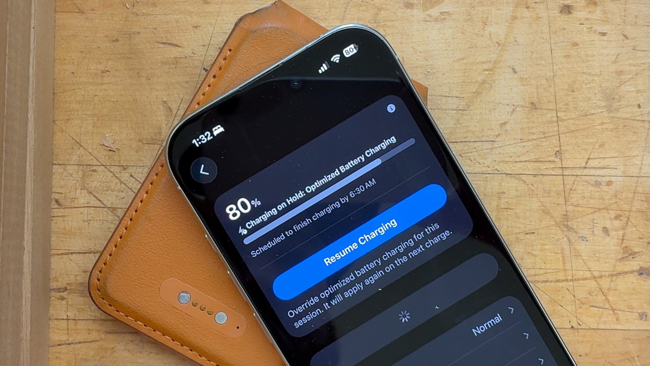 Smartphone on a wooden surface, showing battery status at 80 percent with optimized charging notification on the screen. Brown case partially visible underneath.