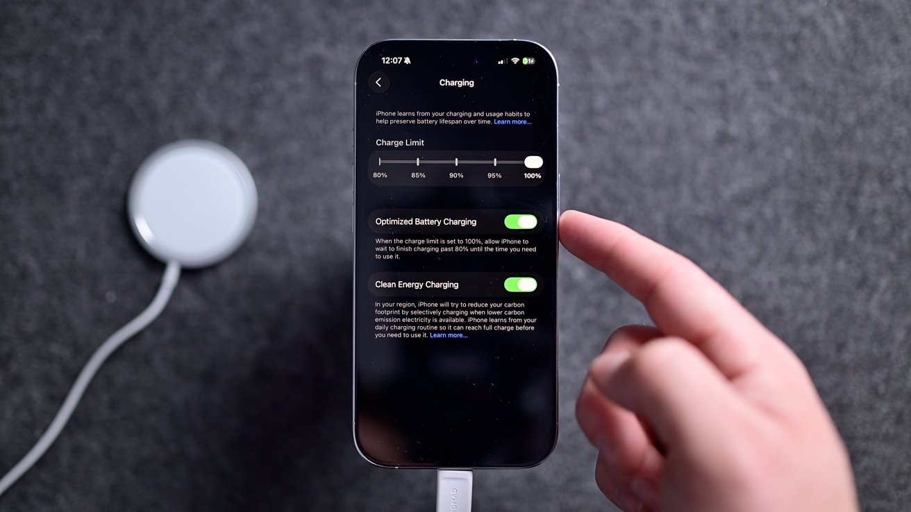 Smartphone charging settings screen with options for charge limit, optimized battery charging, and clean energy charging. A hand points towards the screen. Circular charging pad nearby.