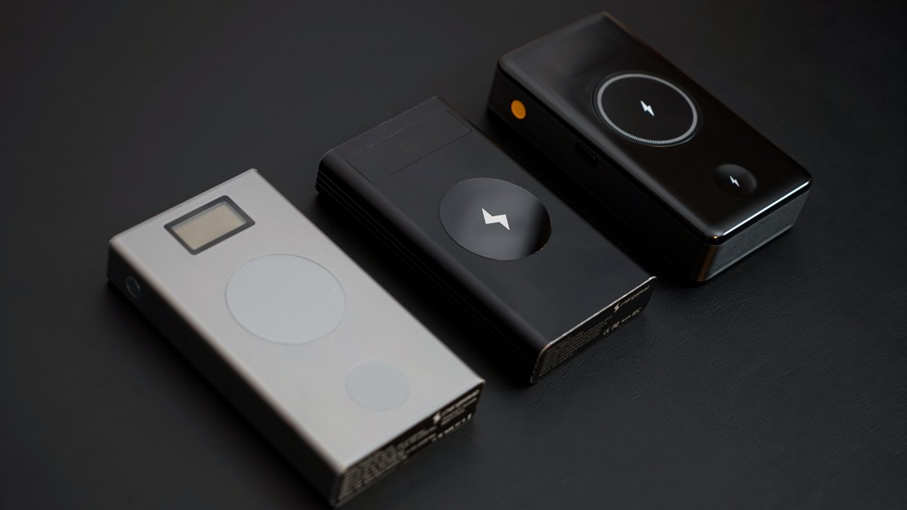 Three sleek power banks in black and silver with circular charging symbols rest on a dark surface.
